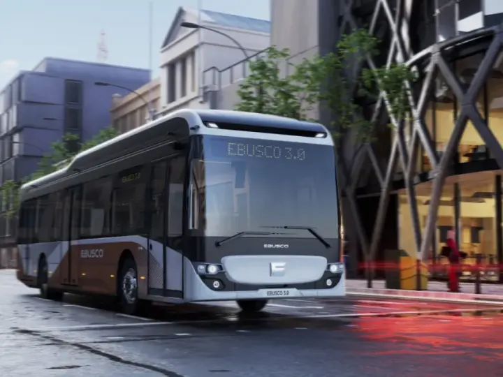 Un bus Ebusco 3.0 moderne circule dans une rue urbaine mouillée, reflétant les lumières de la ville.