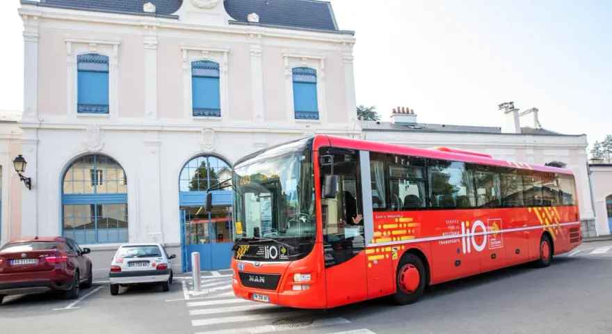 Un bus rouge Lio, service public Occitanie, s'arrête devant une gare.