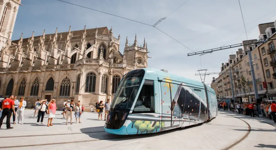 Un tram **Keolis Vélizy** décoré circule devant une cathédrale gothique. Des passants attendent sur le quai.