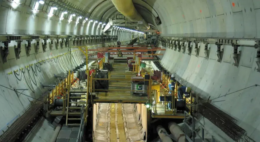 Intérieur d'un tunnel duplex en construction, avec des machines, des ouvriers et des tuyaux.