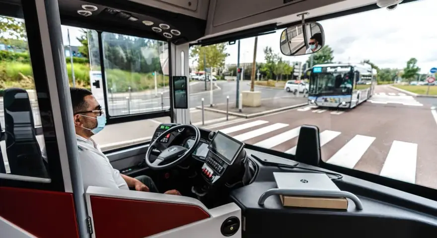 Vue de l'intérieur d'un bus RATP, le conducteur porte un masque. Un autre bus approche au loin.