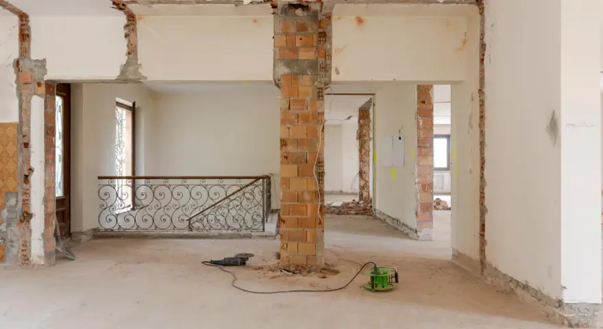 Intérieur en chantier, murs abattus, poutres apparentes. Les outils suggèrent une rénovation, pas une simple réhabilitation.