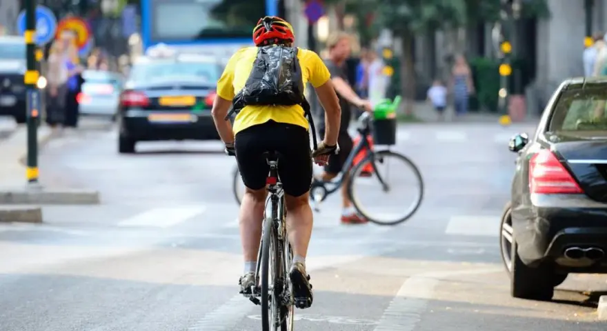 Un cycliste en tenue jaune et casque rouge profite de faire du vélo en ville, traversant une rue animée avec des voitures et un bus.