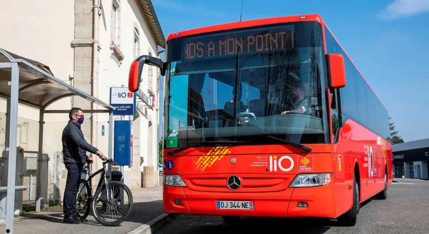 Un homme attend un bus LIO rouge à un arrêt, prêt à monter avec son vélo. Ce bus dessert les lignes comme Graulhet Gaillac.
