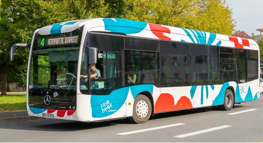 Bus txiktxak Bayonne, ligne 4, direction Aéroport de Biarritz, avec un motif coloré bleu et rouge sur fond blanc.