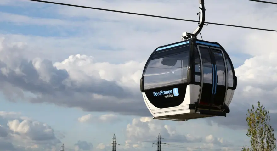 Cabine de téléphérique urbain en France, survolant un paysage urbain sous un ciel nuageux.