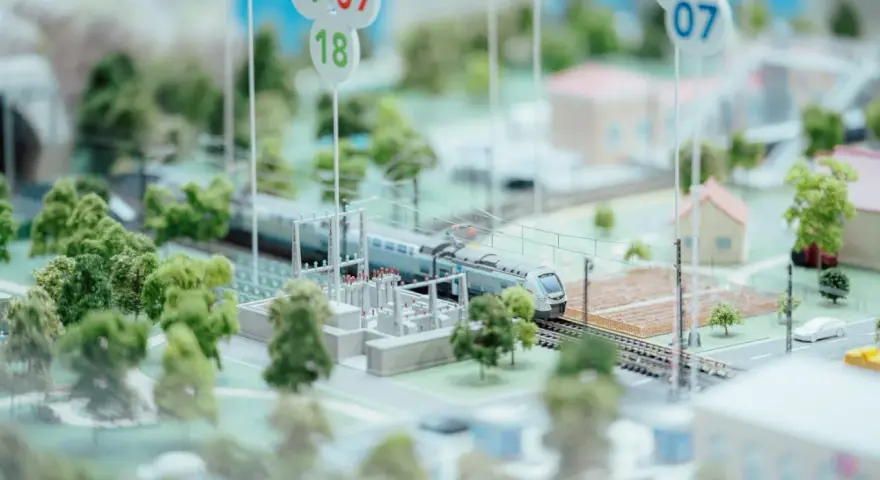 Maquette ferroviaire avec un train, des arbres et des maisons. Des panneaux indiquent des dates, peut-être pour un projet mobco 2026.