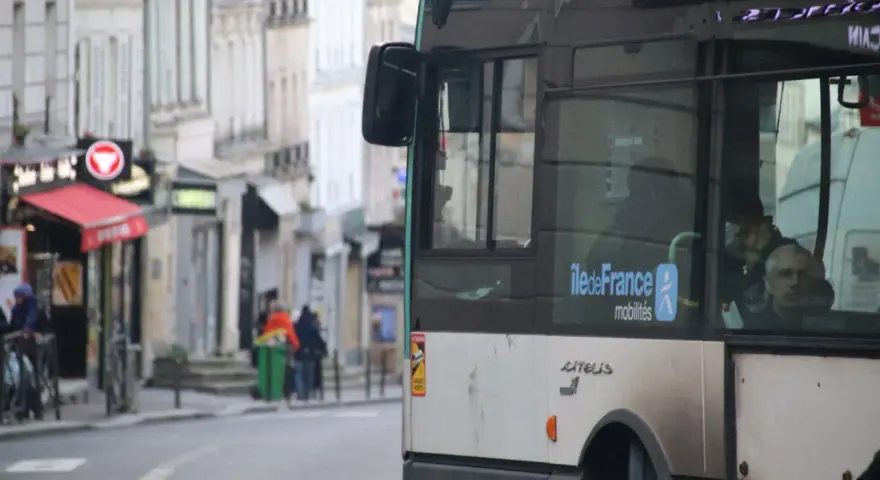 Un nouveau bus RATP, arborant le logo Île-de-France Mobilités, circule dans une rue bordée de bâtiments anciens.