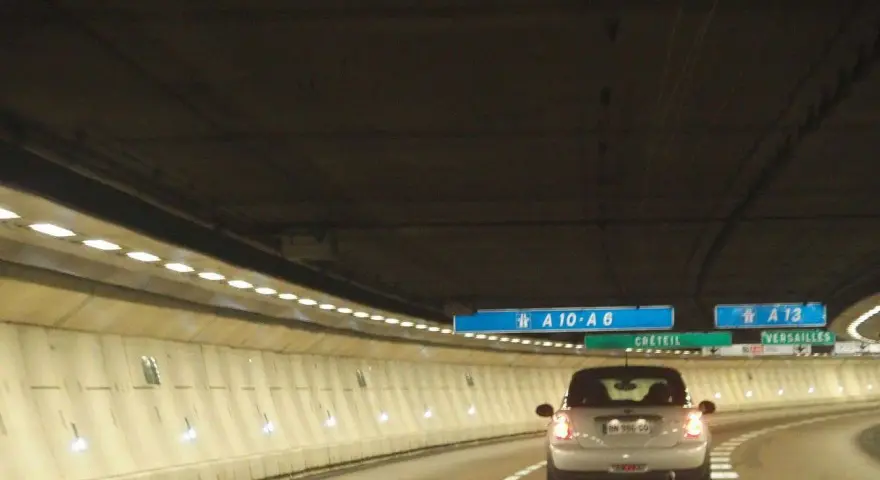 Voiture dans un tunnel éclairé, direction A10-A6 et A13. Un panneau indique Créteil et Versailles. Passage d'un duplex péage.