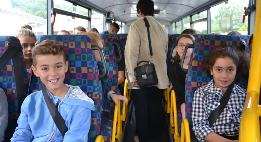 Des enfants souriants et une adulte voyagent dans un autobus scolaire aux sièges colorés.