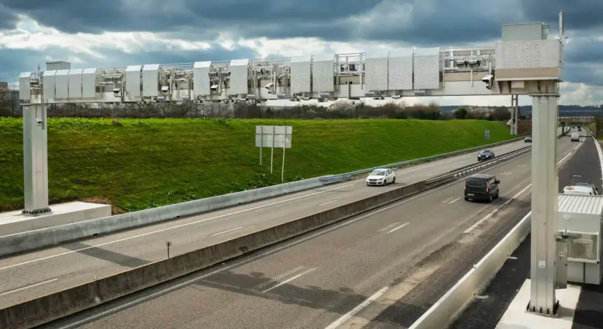 Portique de péage urbain sur une autoroute, avec des voitures passant sous les caméras.