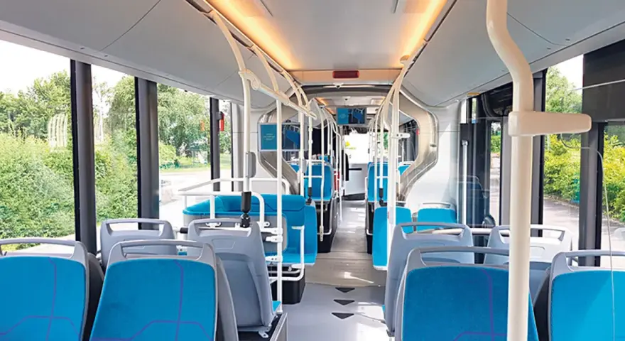 Intérieur d'un bus IDFM moderne avec des sièges bleus et gris, des barres de maintien et de grandes fenêtres donnant sur la verdure.