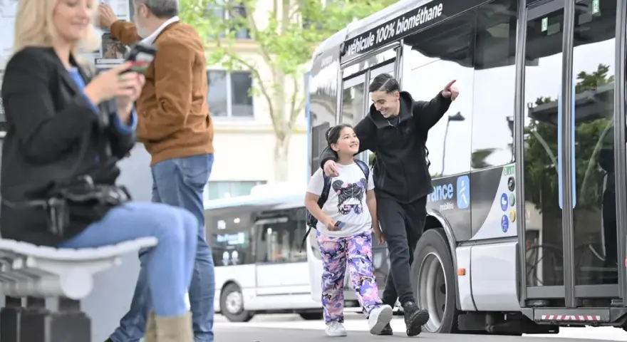 Un jeune homme et une fillette souriants marchent près d'un bus Transdev à Blois.