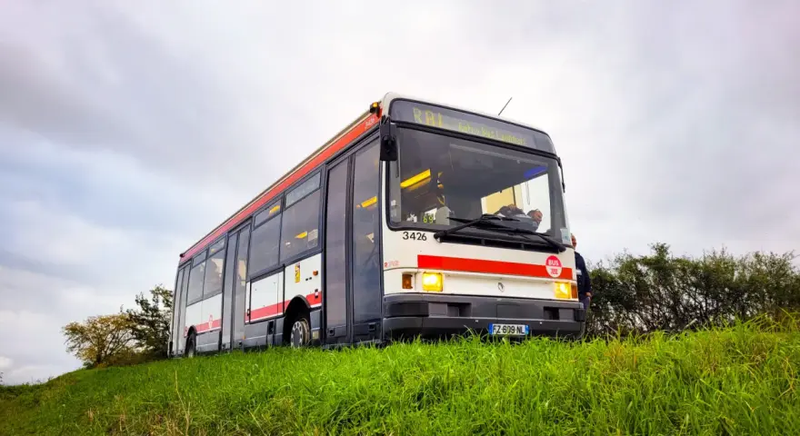 Un bus Renault R312 blanc et rouge, immatriculé FZ-609-NL, roule sur une colline herbeuse sous un ciel couvert.