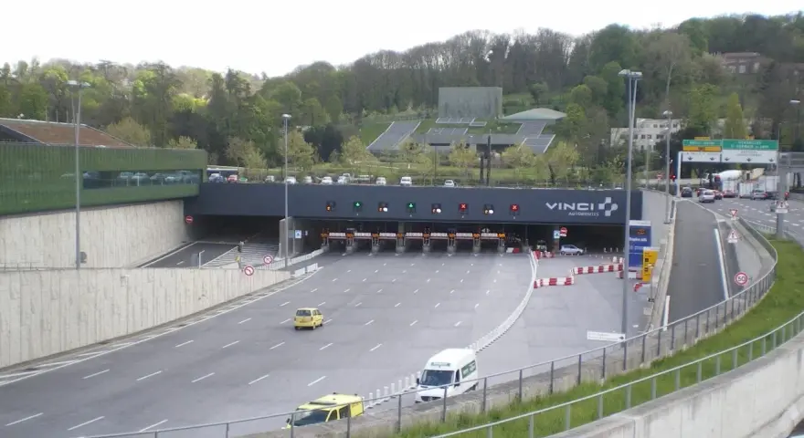 Entrée d'un **duplex autoroute** Vinci. Des voitures et des camions passent sous des portiques de péage.
