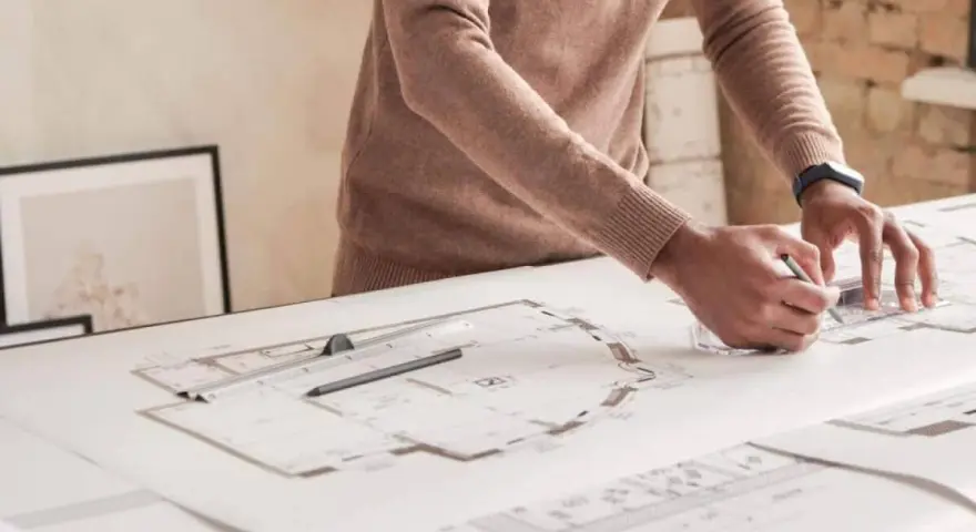 Un architecte dessine des plans détaillés, traçant des lignes précises pour un projet. Il y a plu trappes sur la table.