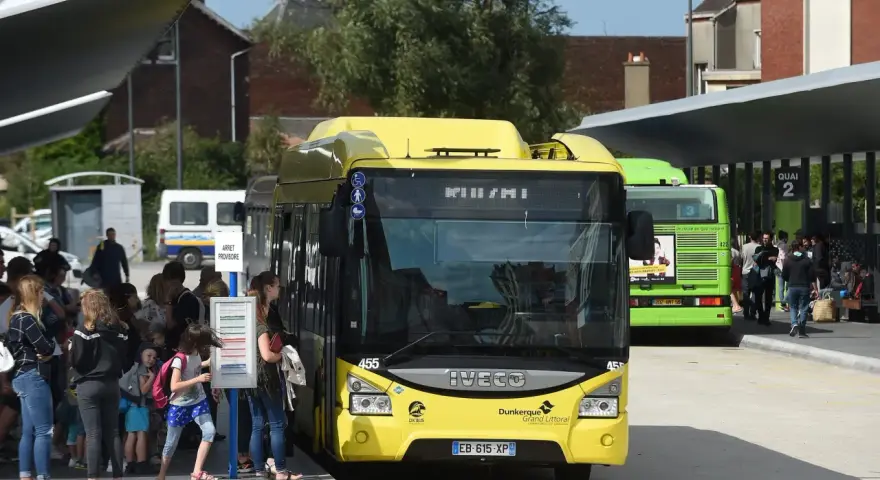 Des bus jaunes et verts attendent des passagers. Une affiche sur le bus vert mentionne "100% GRATUIT", illustrant la gratuité des transports en commun.