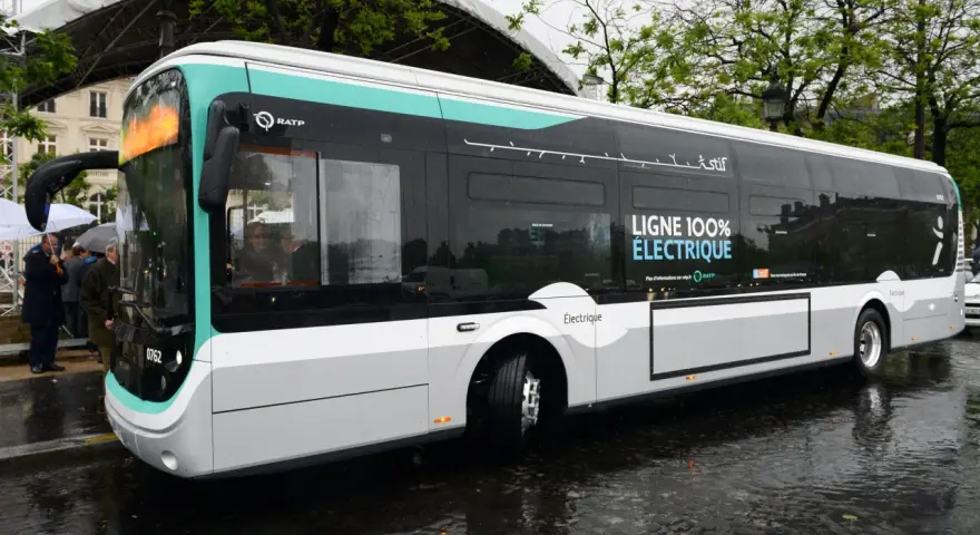 Un bus RATP bleu et blanc, "LIGNE 100% ÉLECTRIQUE", roule sur une chaussée mouillée.