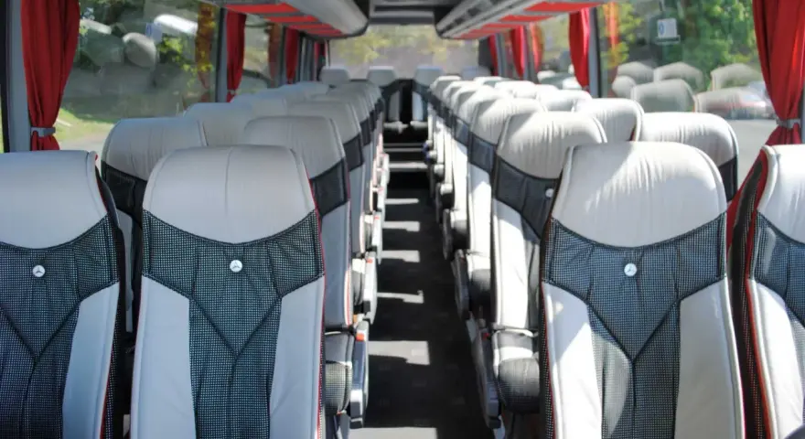 Intérieur d'un tour bus avec des sièges confortables et des rideaux rouges.