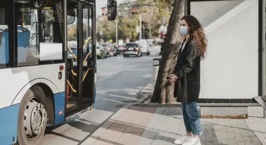 Une jeune femme avec un masque attend le bus, un moyen de déplacement pratique en ville.