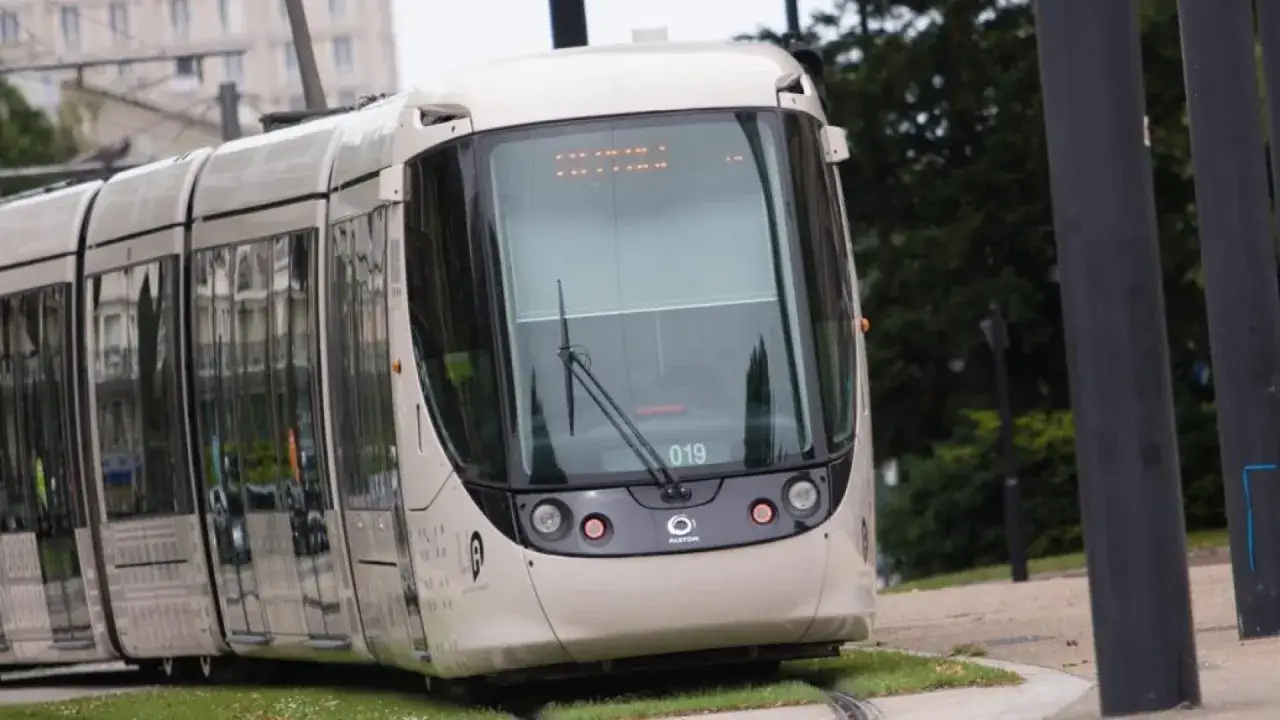 Un tram moderne de Transdev Normandie circule sur ses rails, refl&eacute;tant le paysage urbain dans ses vitres.