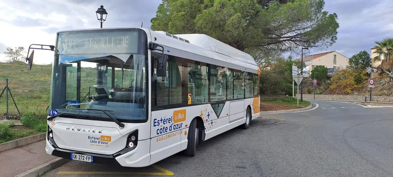 Un bus blanc de l'Estérel Côte d'Azur circule sur une route sinueuse, sous un ciel nuageux.