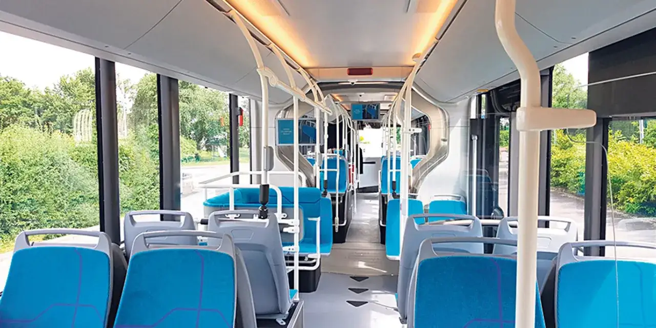 Intérieur d'un bus IDFM moderne avec des sièges bleus et gris, des barres de maintien et de grandes fenêtres donnant sur la verdure.