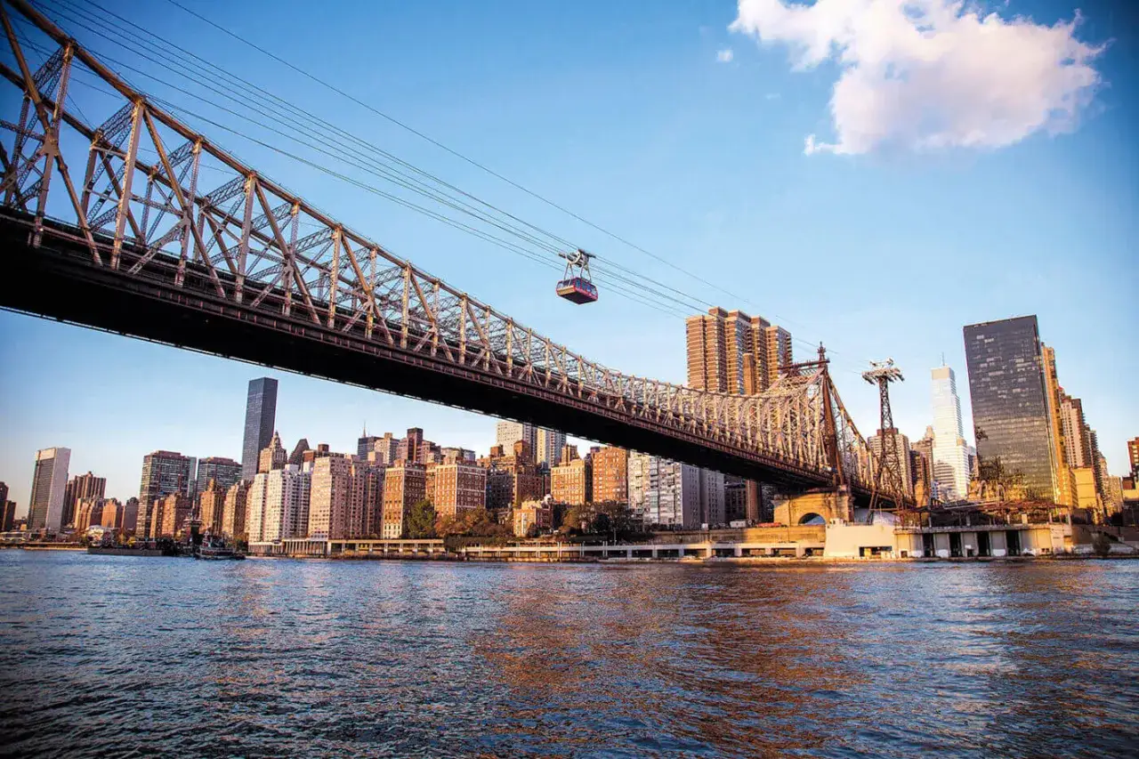 Le téléphérique au-dessus de l'eau, sous un pont imposant, illustre la mobilité urbaine définition, reliant les gratte-ciel de New York.