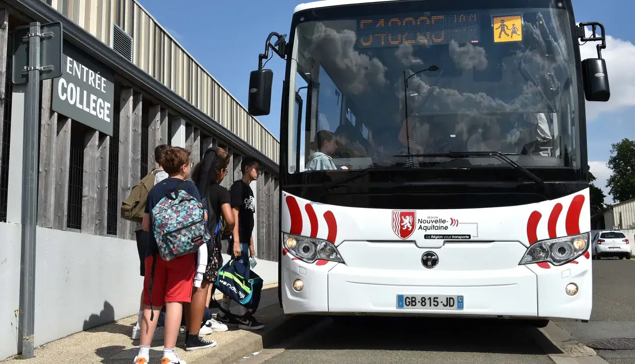 Des élèves attendent leur autobus scolaire devant un collège.
