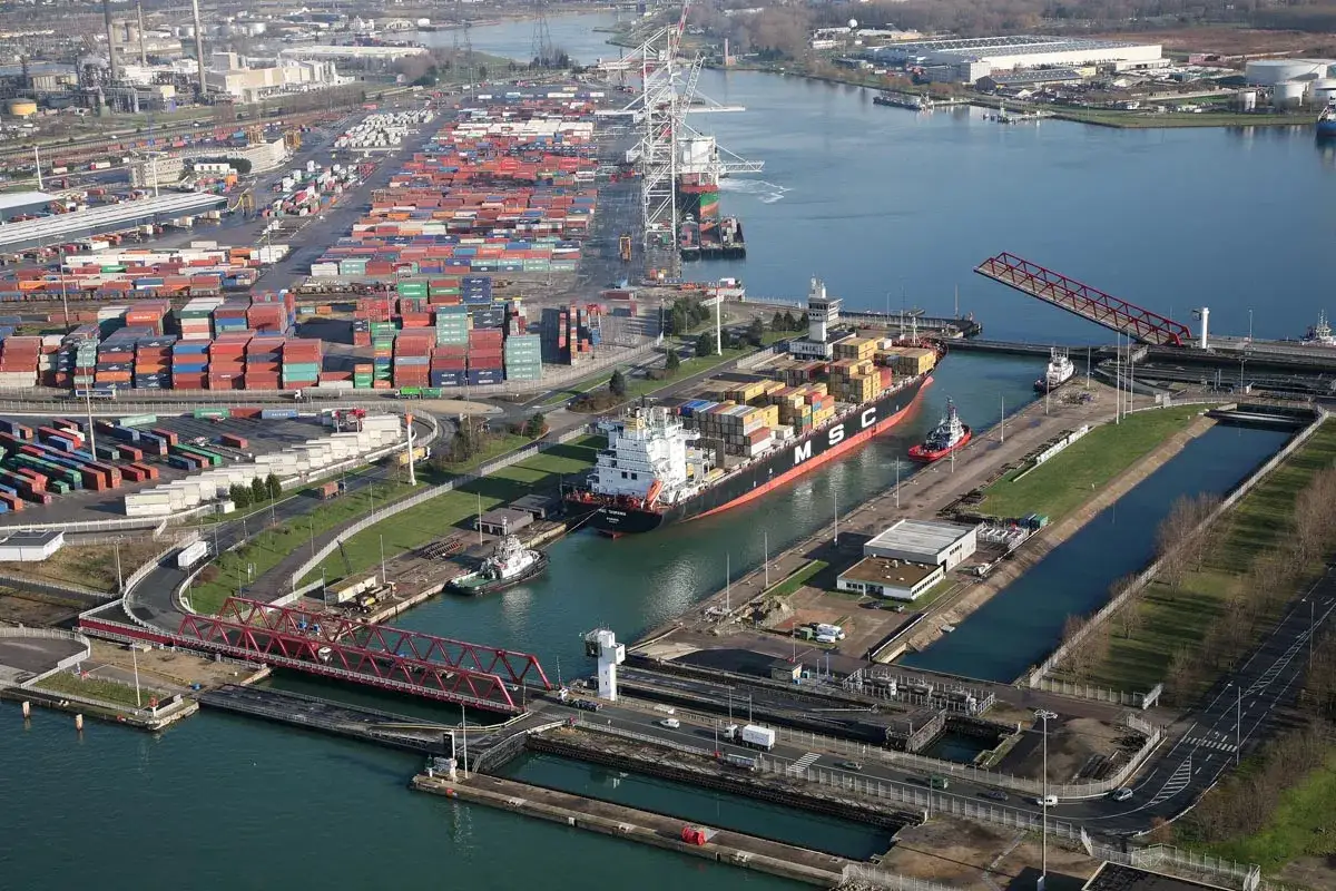 Vue aérienne d'un port maritime avec des conteneurs empilés, un porte-conteneurs MSC, des remorqueurs et des infrastructures de navigation, dont un pont-levis.