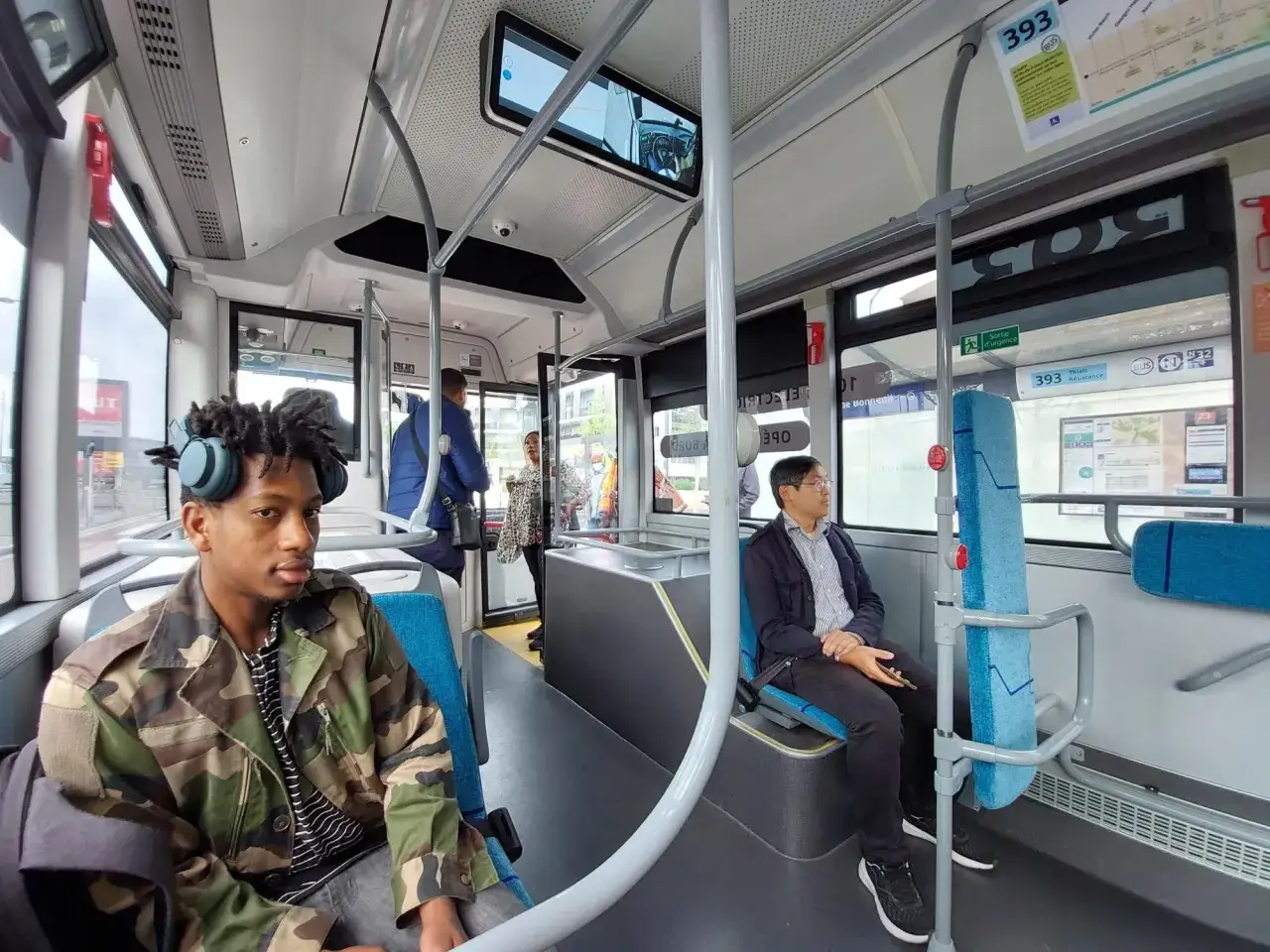 Voyagez confortablement en bus. Un jeune homme aux écouteurs bleus est assis à l'avant, tandis que d'autres passagers se détendent.