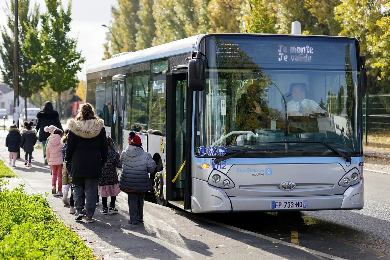 Des enfants montent dans un bus Keolis, accompagnés par des adultes. Le chauffeur salue.