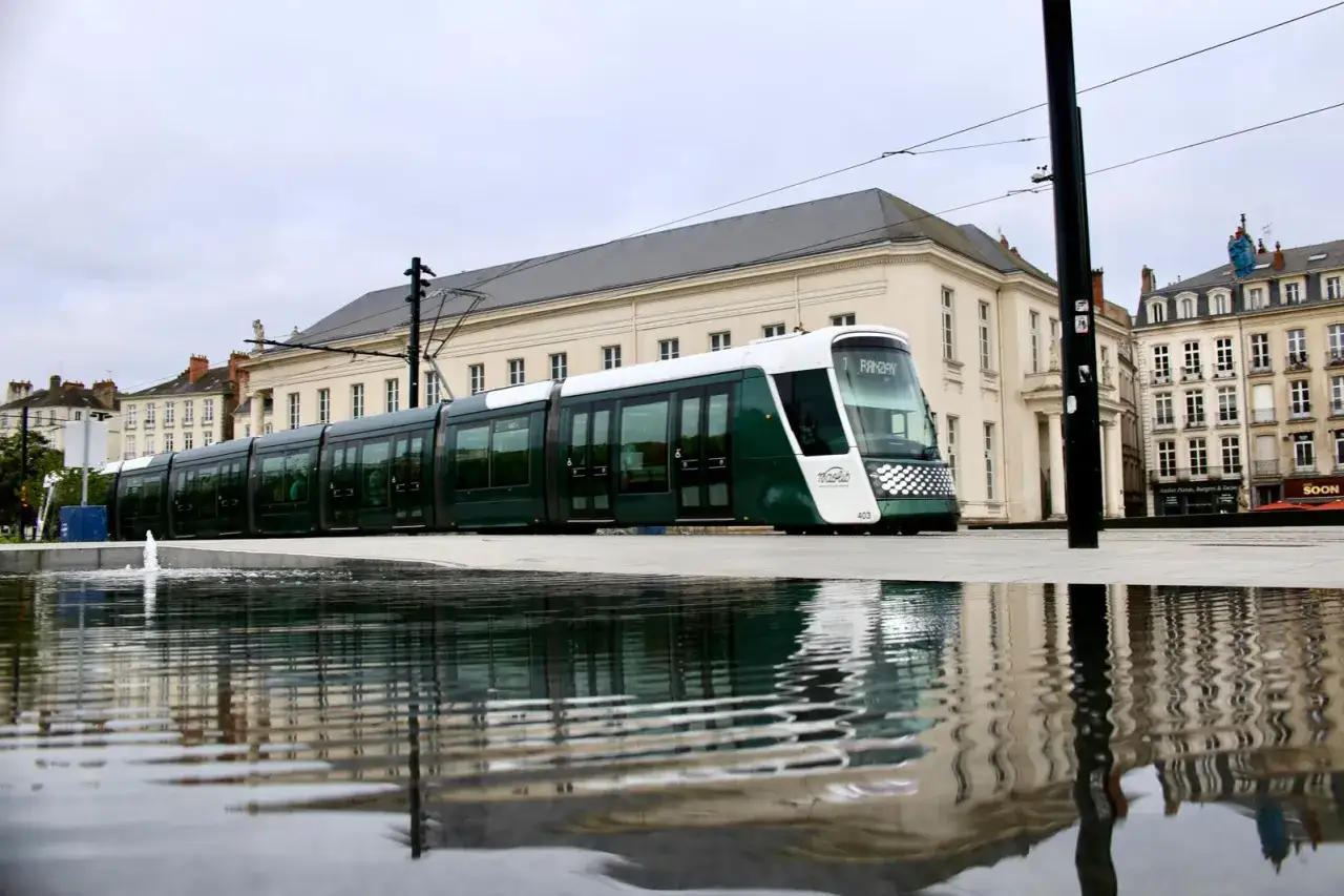 Un tram vert et blanc à Nantes, reflété dans l'eau. Parfait pour un week-end d'exploration.