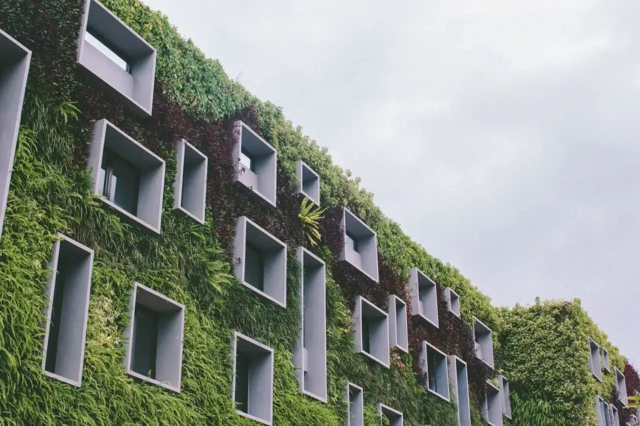 Un bâtiment à la façade végétalisée, avec des fenêtres carrées qui semblent s'ouvrir sur une ville circulaire imaginaire.