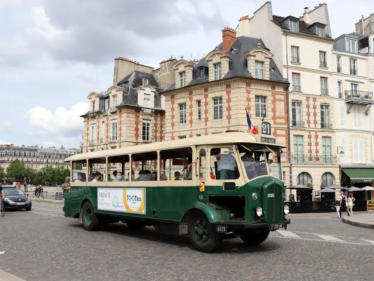 Un autobus Renault vintage vert et crème circule dans une rue pavée de Paris, transportant des touristes.