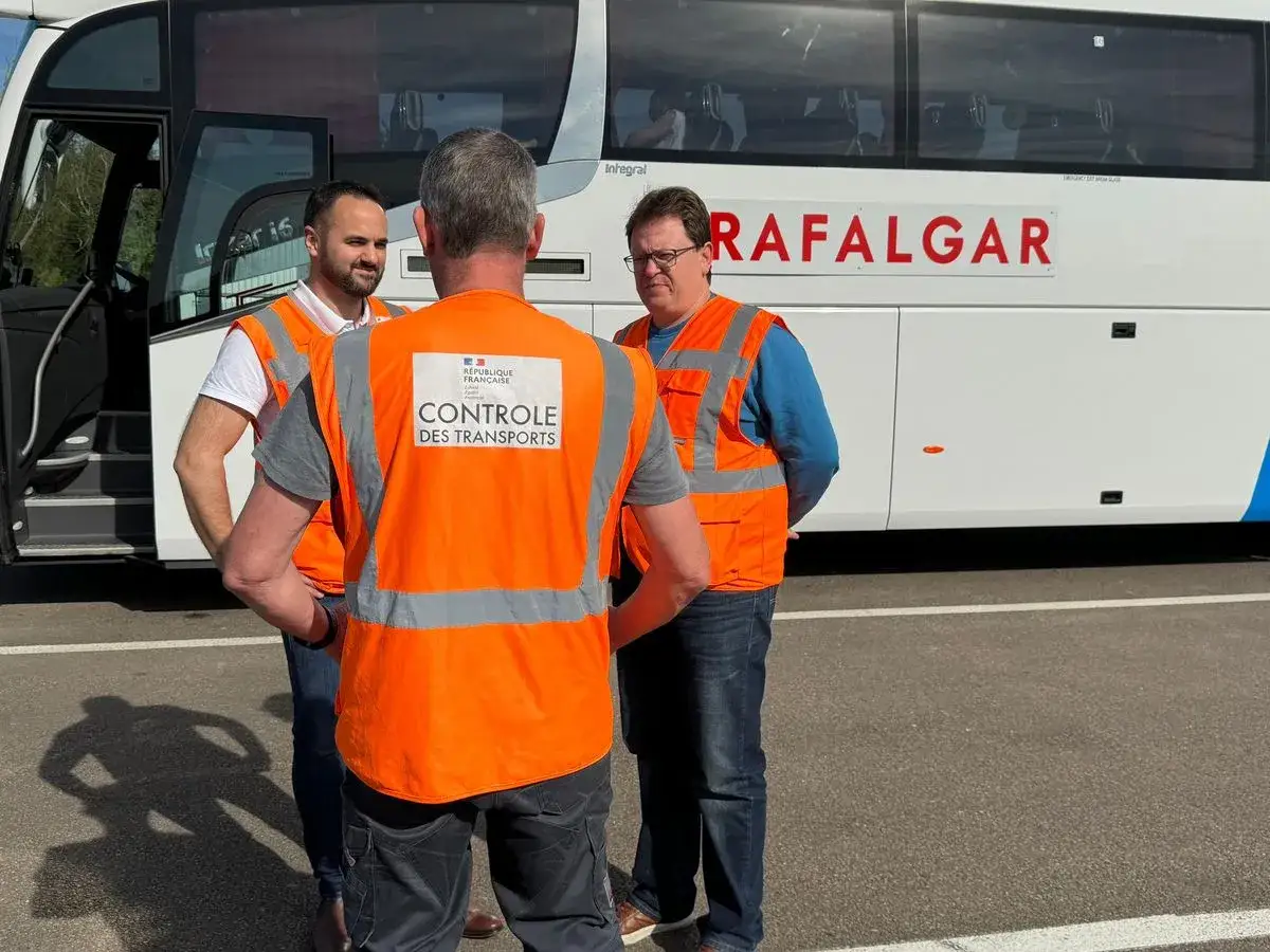 Trois hommes en gilets orange de contr&ocirc;le des transports discutent pr&egrave;s d'un bus. L'un d'eux porte un gilet avec l'inscription 