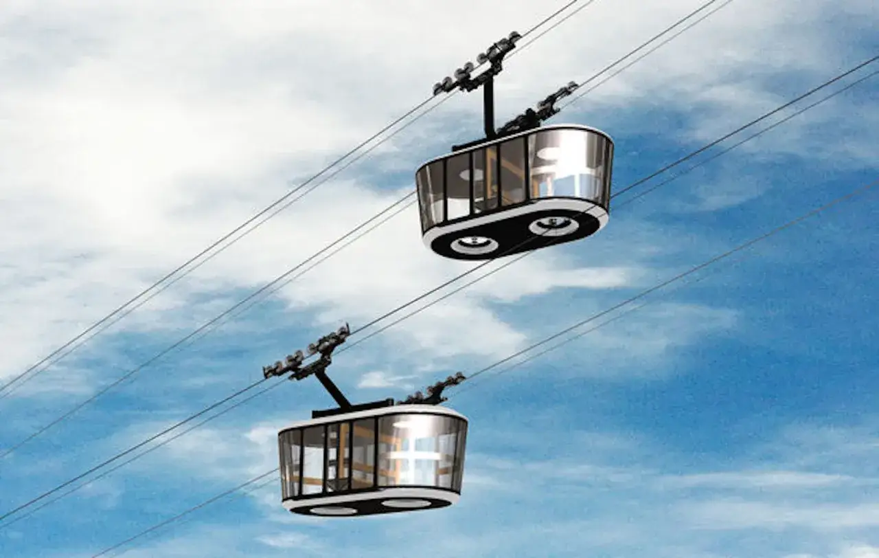 Deux cabines modernes de téléphérique urbain glissent sur des câbles, offrant une vue panoramique sur le ciel bleu et nuageux.