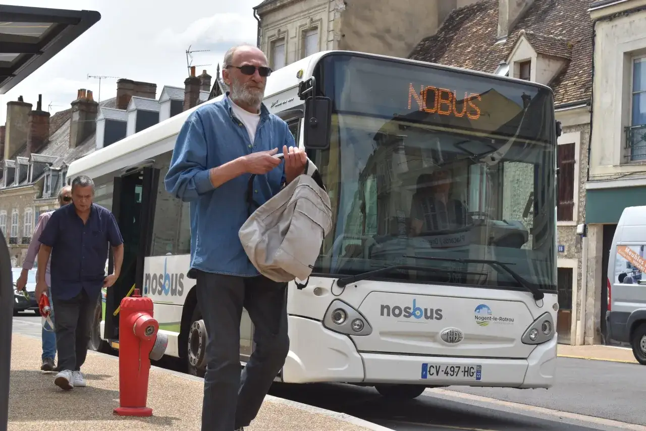 Un homme attend le bus &agrave; Nogent-le-Rotrou, sac &agrave; la main. Le panneau lumineux indique 