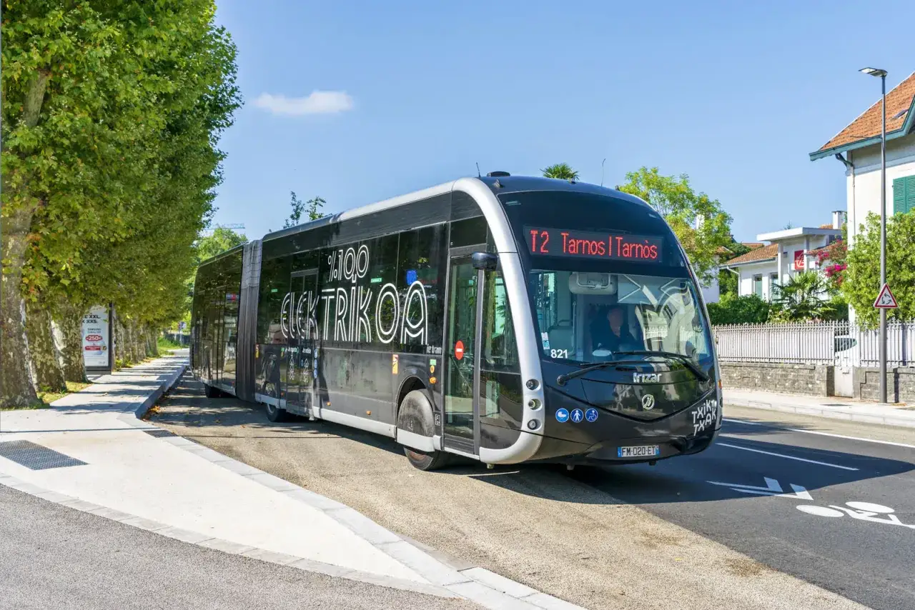 Un bus électrique %100 ELEKTRIKOA de Txiktxak Bayonne circule sur une route ensoleillée.