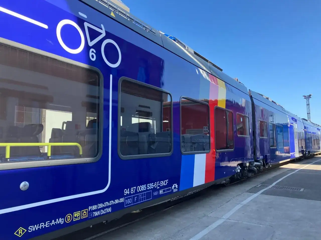 Un train régional bleu vif avec un logo de vélo et des bandes colorées.