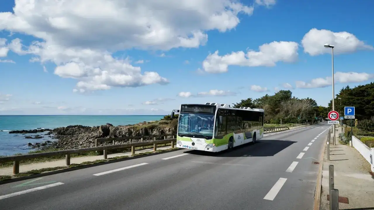 Un bus LILA circule sur une route côtière près de Guérande, avec la mer et des nuages en arrière-plan.