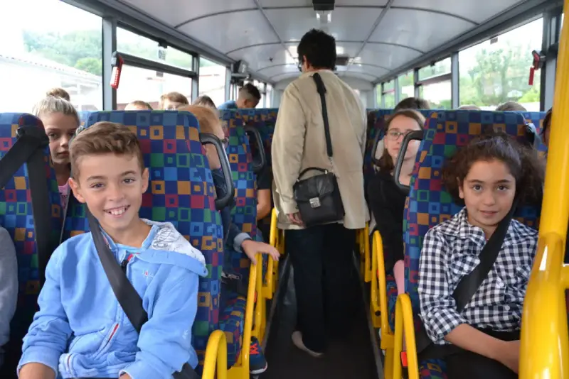 Des enfants souriants et une adulte voyagent dans un autobus scolaire aux sièges colorés.
